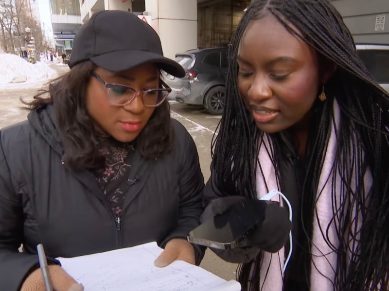 Two people standing close together while one holds a phone and the other a piece a paper while they listen to the conversation.