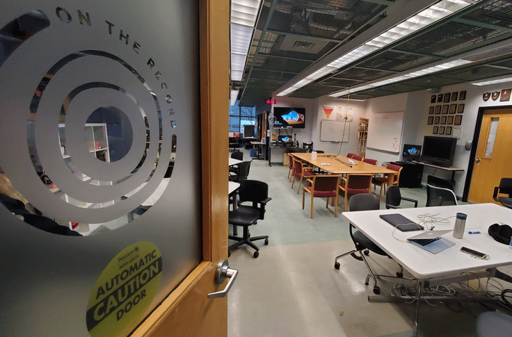 The door of the On the Record newsroom is half open shoing the desks and workspace in the classroom