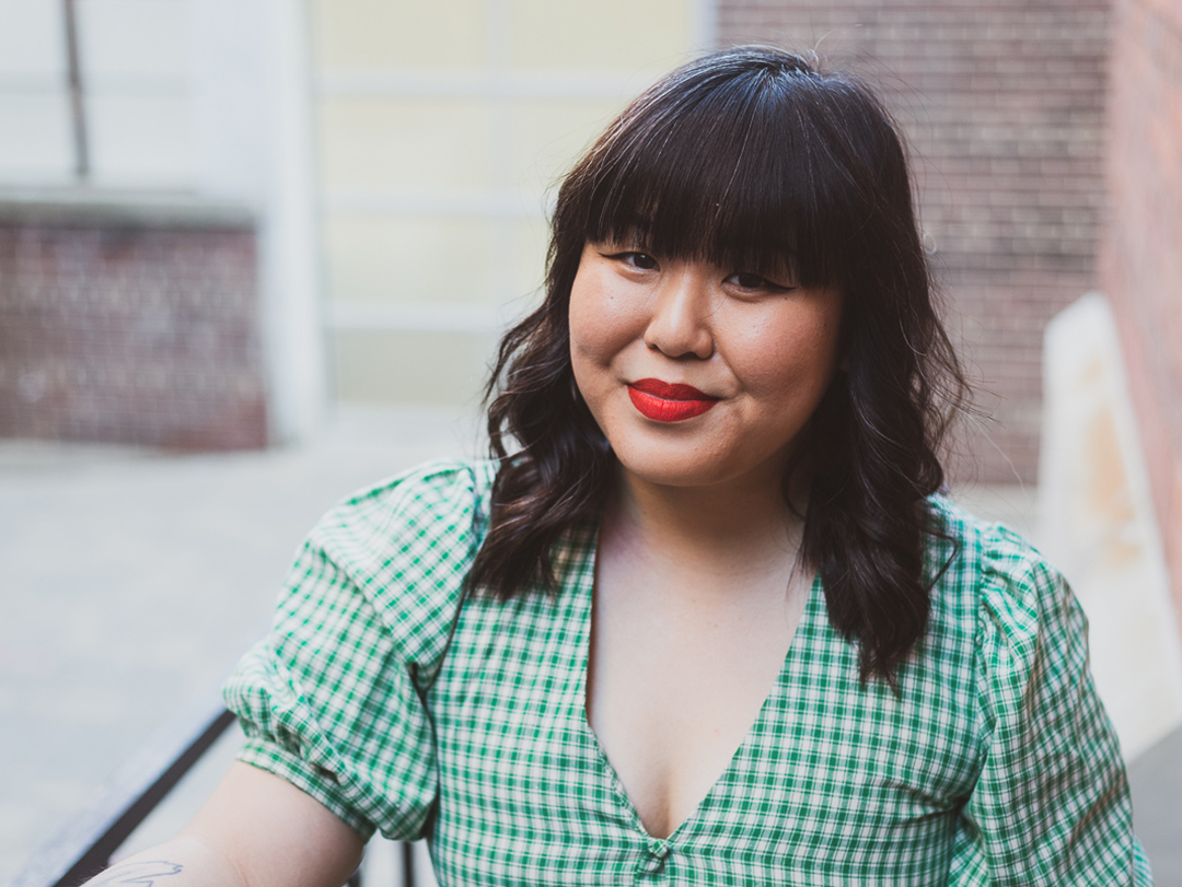 Head shot of Melody Lau who is wearing a green dress and standing in front of a brick background.