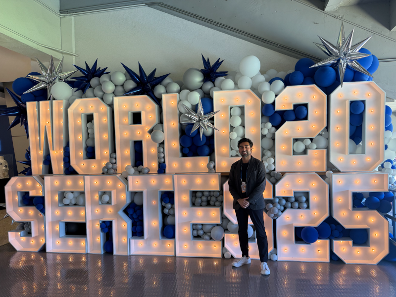 A male alumni stands in front of photo display of big light up letters that say "World Series 2025."