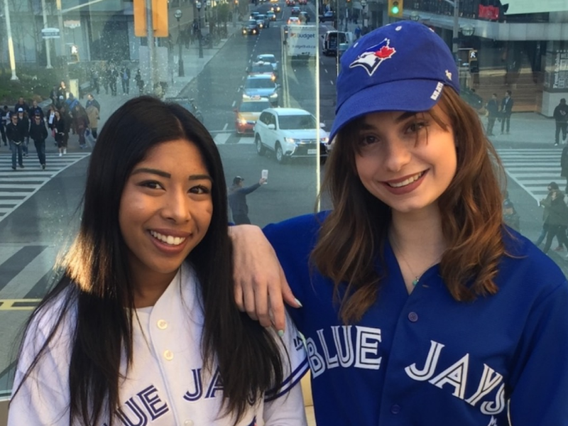Two female alumni wear Blue Jays merch while smiling at the camera.