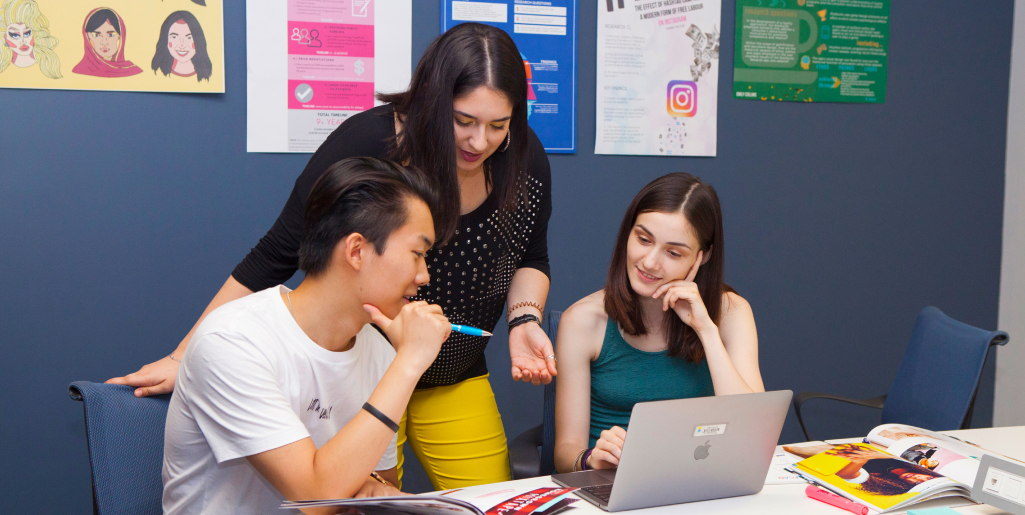 Three students looking at a computer and discussing a topic
