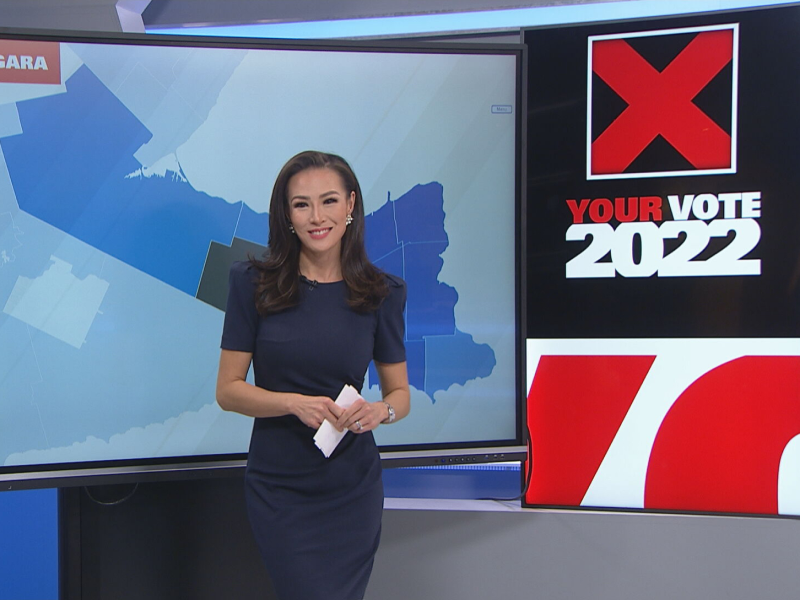 Jennifer Hsiung looks at the camera while reporting the news in front of a backdrop reading, "Your Vote 2022"