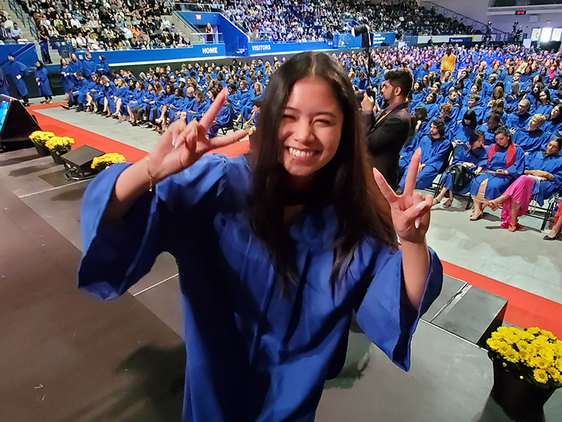 School of Journalism 2023 graduate holds up peace signs while on stage.