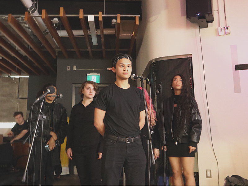 A group of students stand together facing mics during a performance.