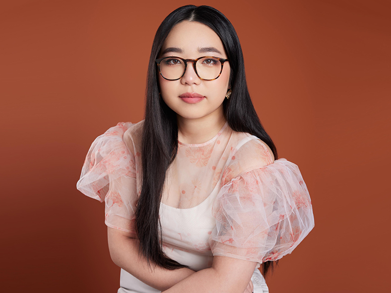 Third-year journalism student Haley Sengsavanh in a pink dress against a burnt orange background.