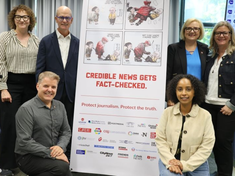 A group of people gather in front of a banner to promote fact checking smile at the camera.