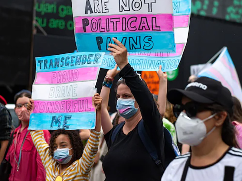 People wearing face masks at a trans rights protest holding signs