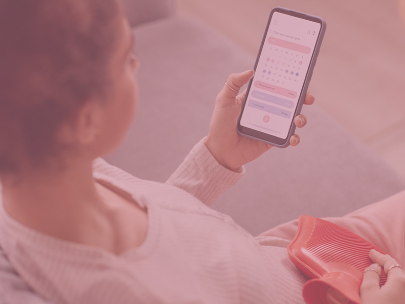 Woman using the Flo app while holding a hot water bottle on her lap