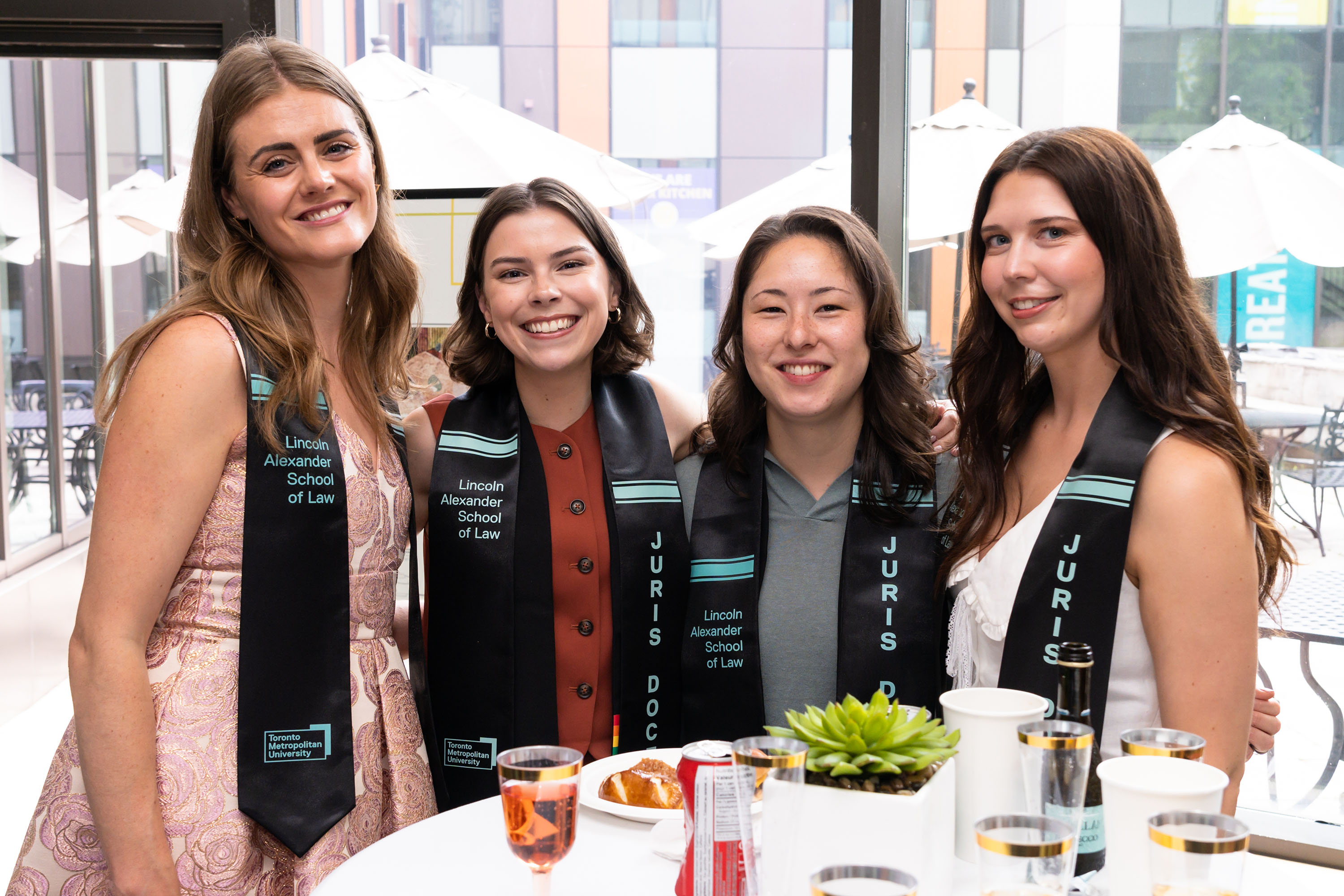 group of four graduates stand smiling around a table for a photo