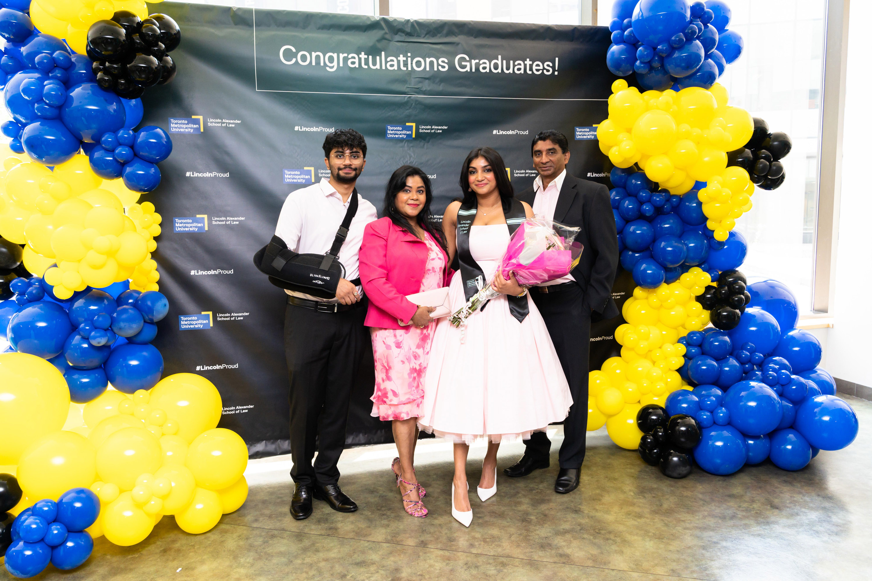 a grad student and their family pose beside balloons at grad celebration