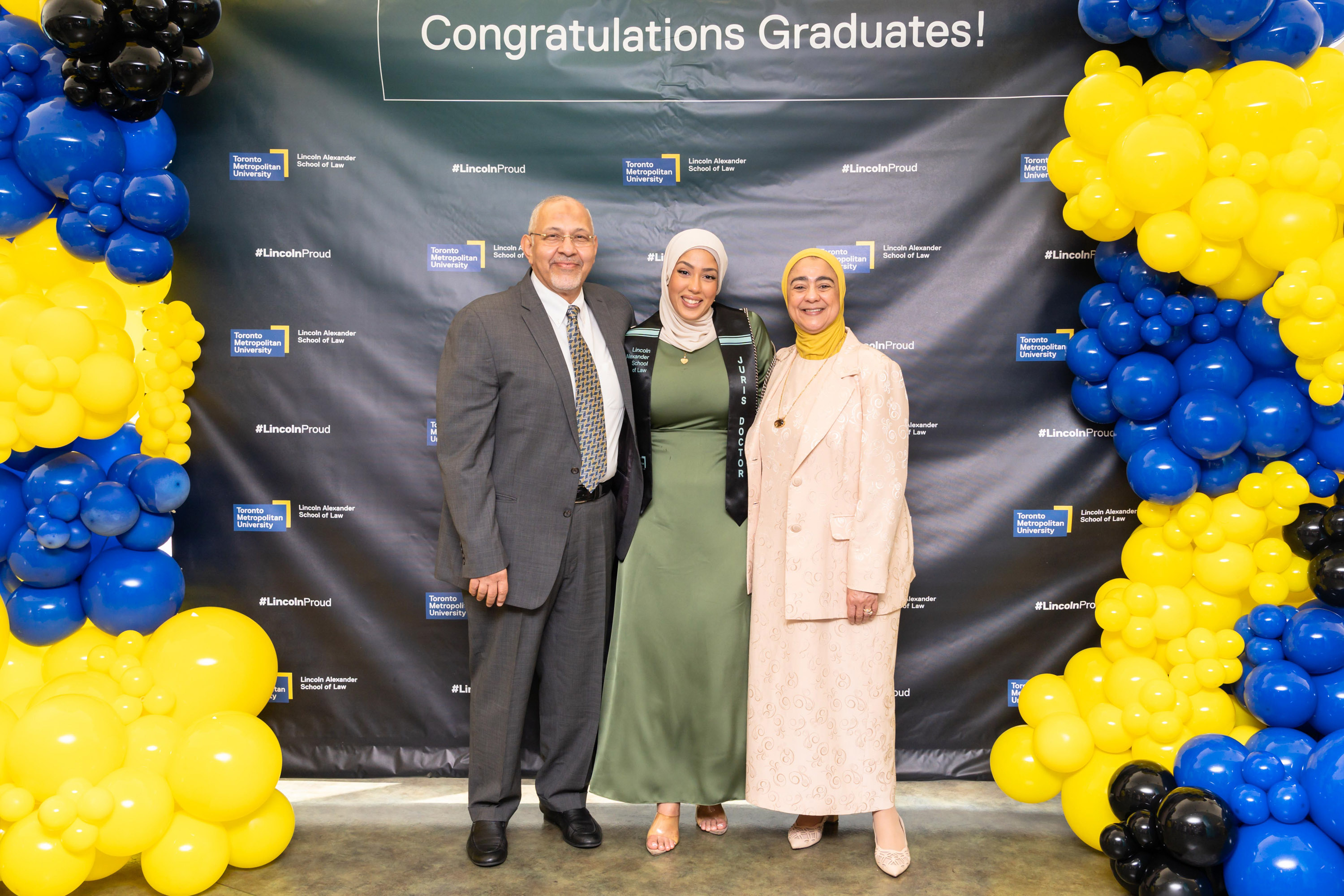 daughter with parents posing at balloon backdrop