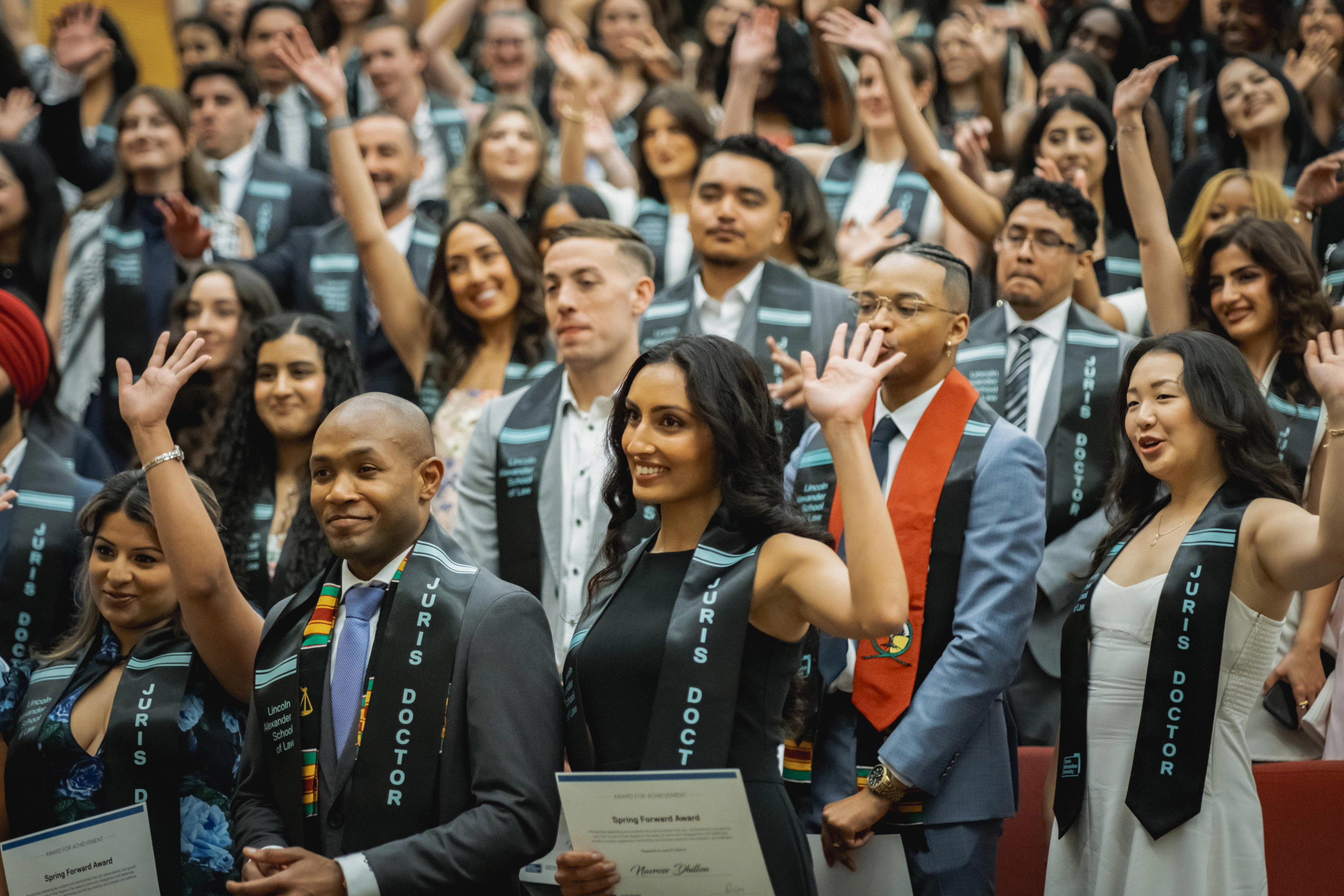 audience of grads raising hands in auditorium