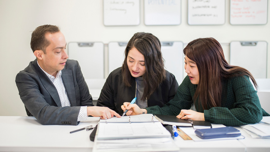 three people reviewing books and materials at a desk