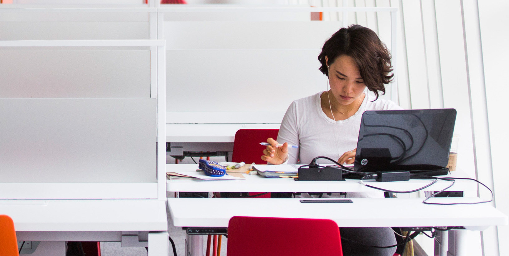 Woman with short hair wearing earphones sits at a desk studying on her laptop