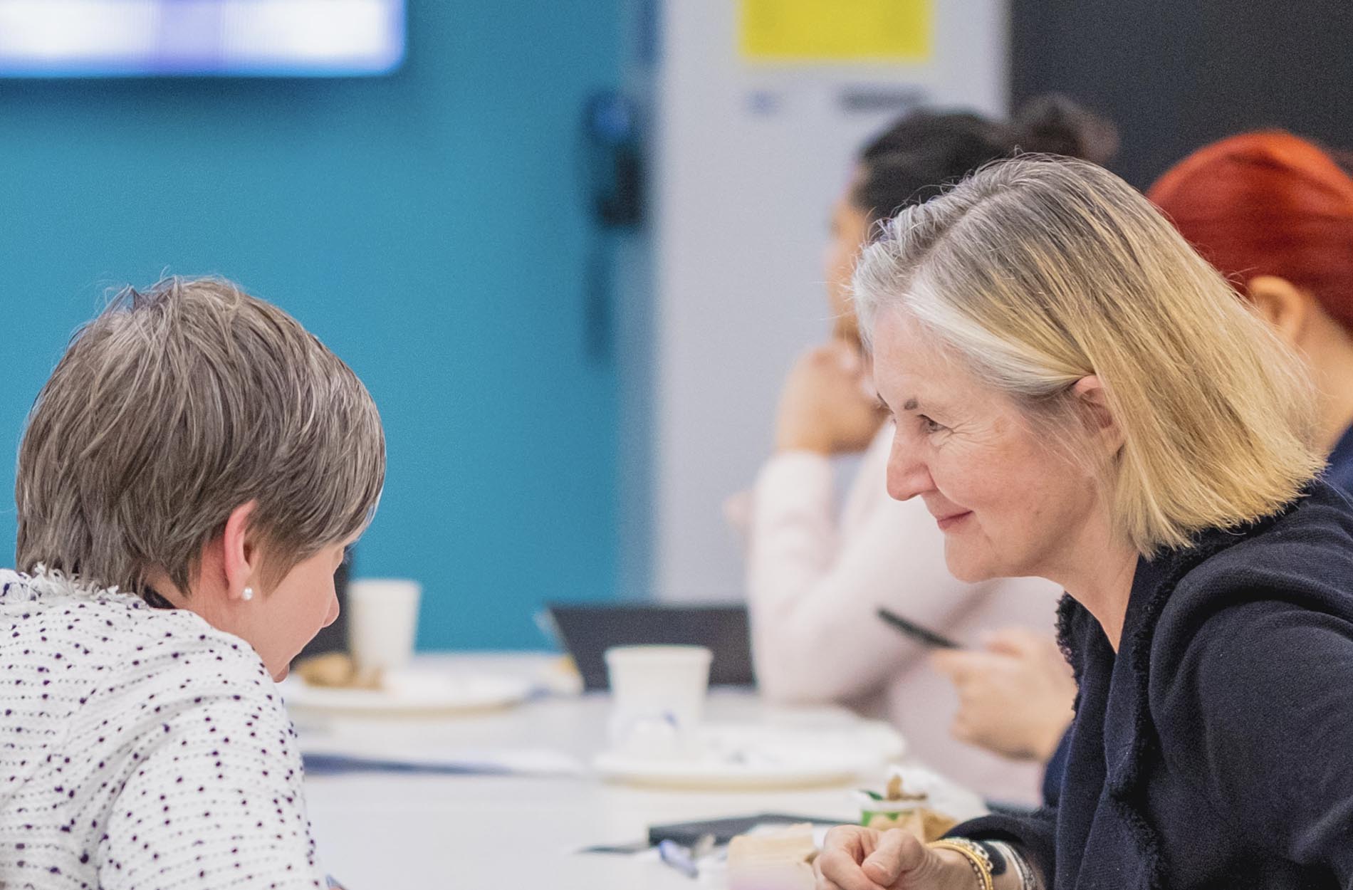 Two conference attendees smile and converse with each other at a table during a workshop
