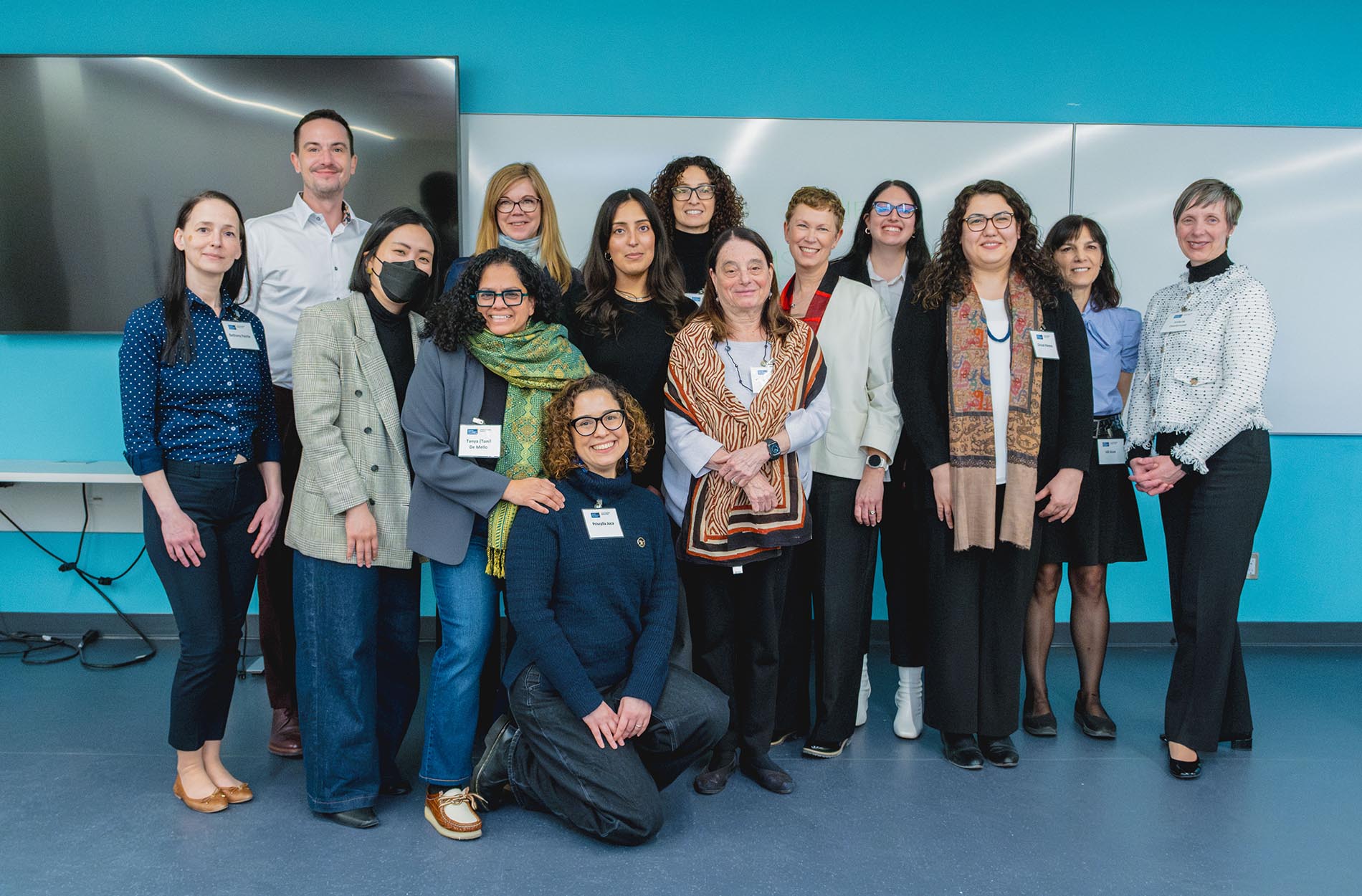 A large group of conference presenters and organizers pose together for a group photo in front of a blue wall