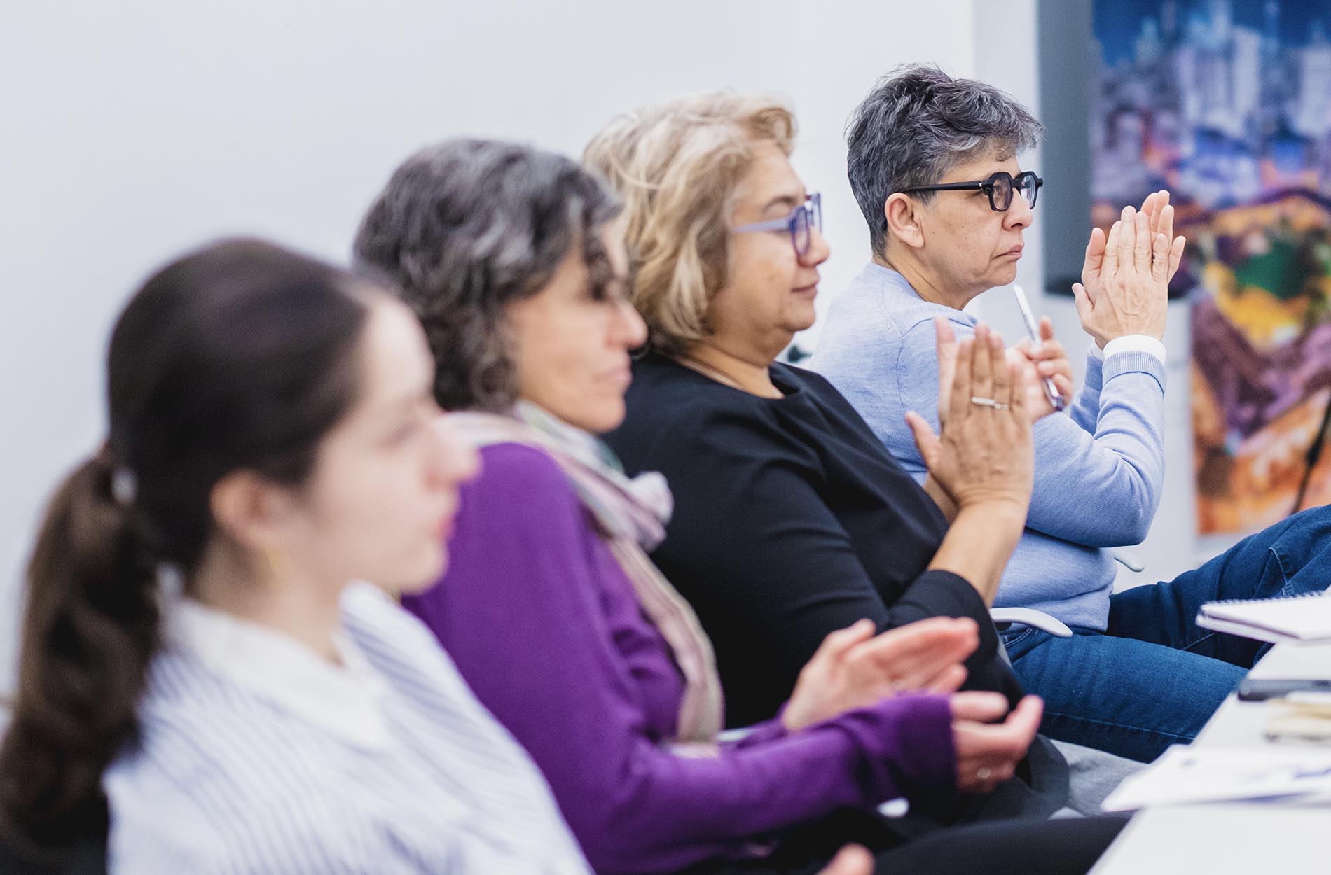 A row of seated conference attendees clap their hands in applause during a presentation