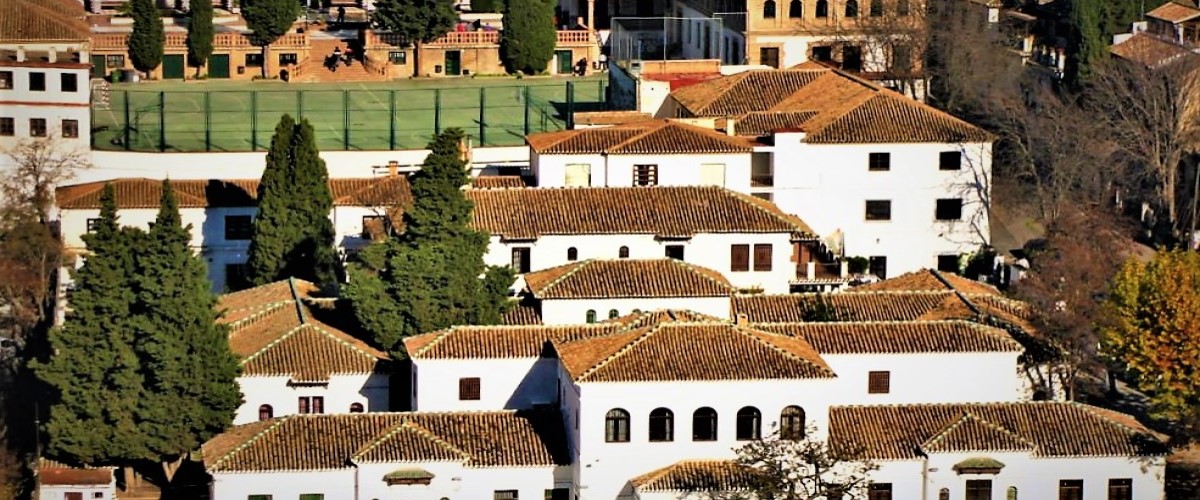 A neighbourhood in Granada, Spain, seen from above, showing white houses, trees and a soccer field.