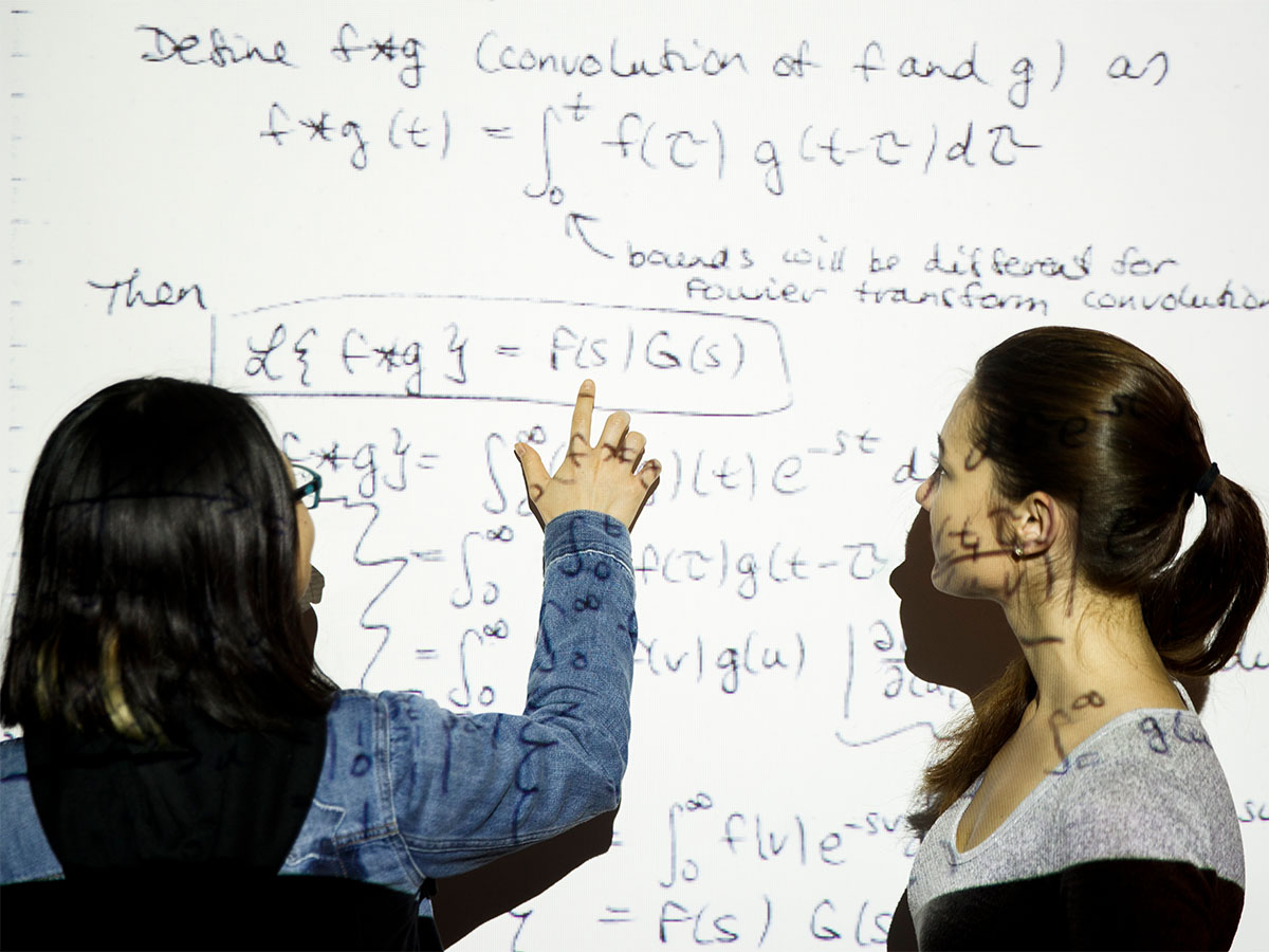 Two students looking at a white board with equations projected on them