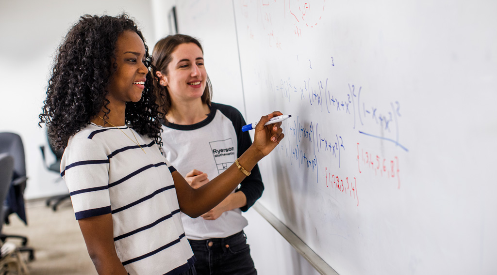 Mathematics undergraduate students working on whiteboard equation.