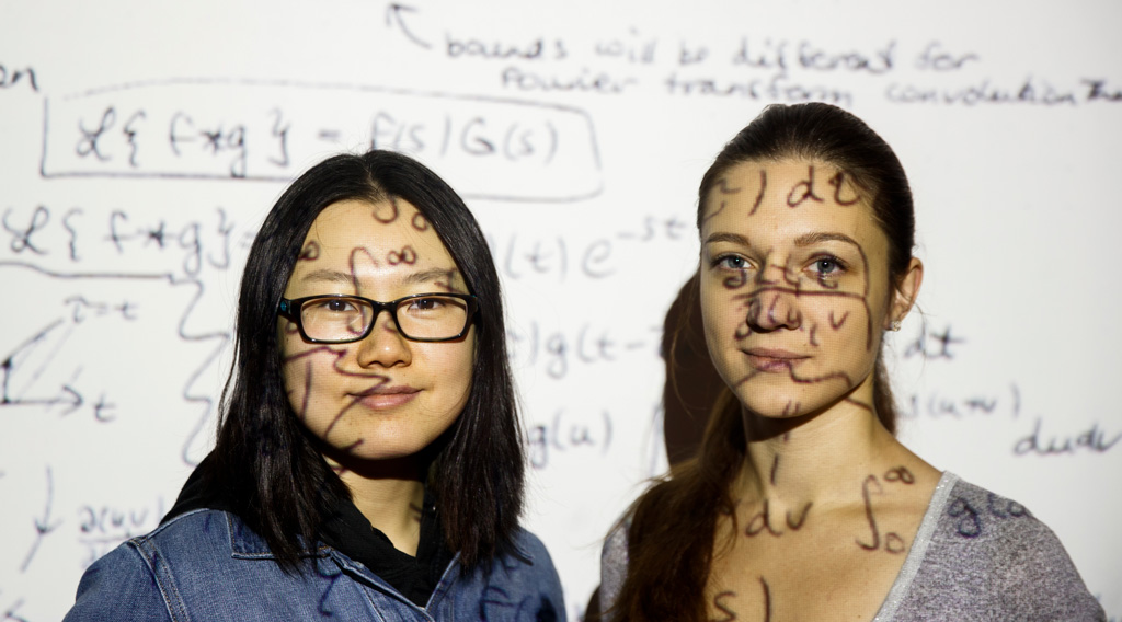 Math graduate students stadning in front of overhead projector with equation shadows over their faces.