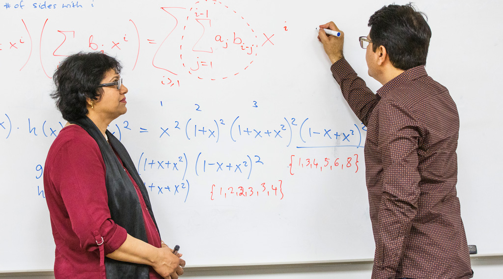 Mathematics graduate studies students working on whiteboard equation.