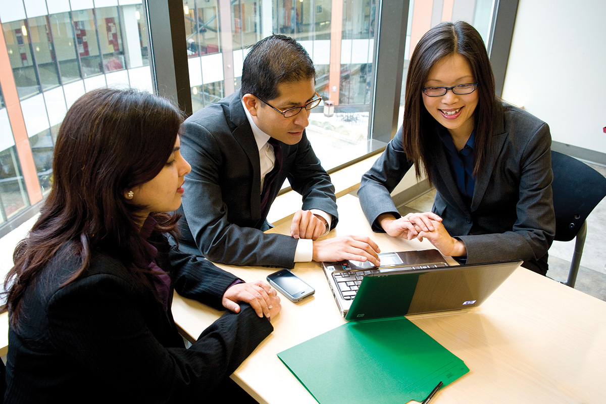 group of three MBA students at a table looking at laptop 