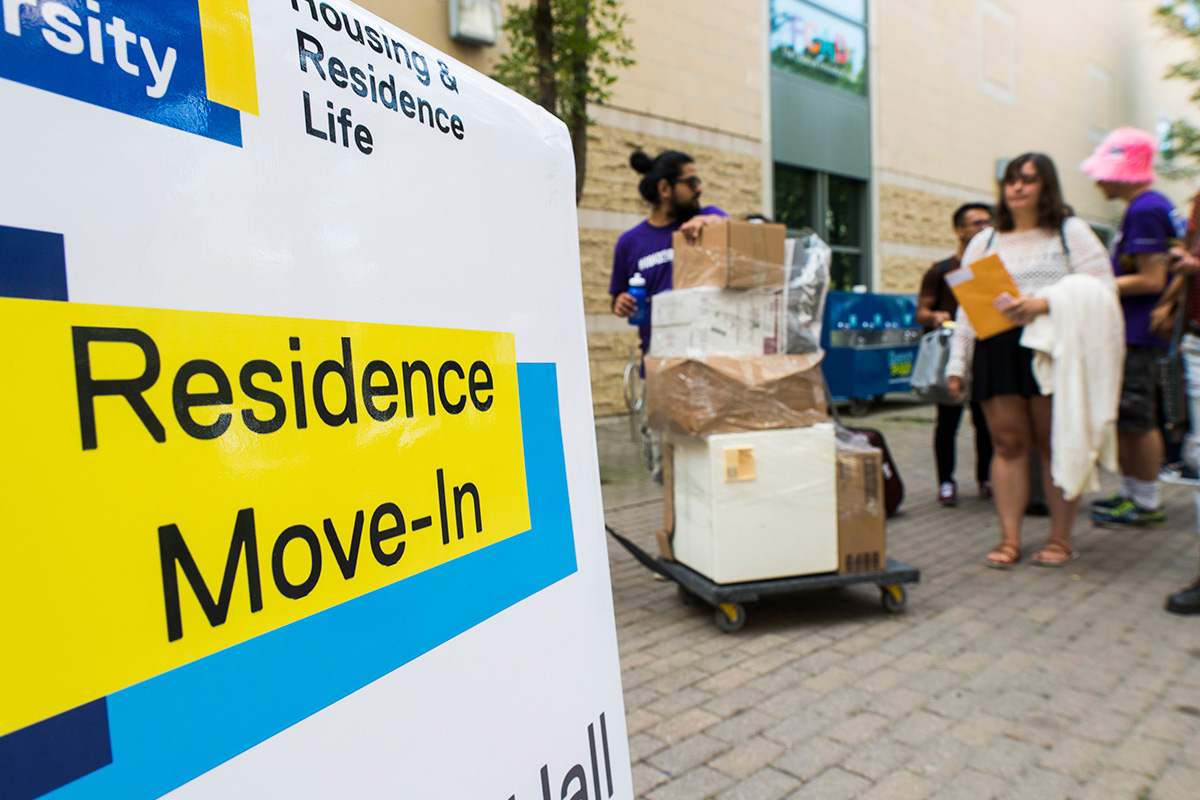 Picture of sign says Residence move-in with students moving in on background