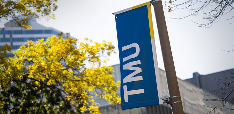TMU campus banner hanging beside trees and university buildings.