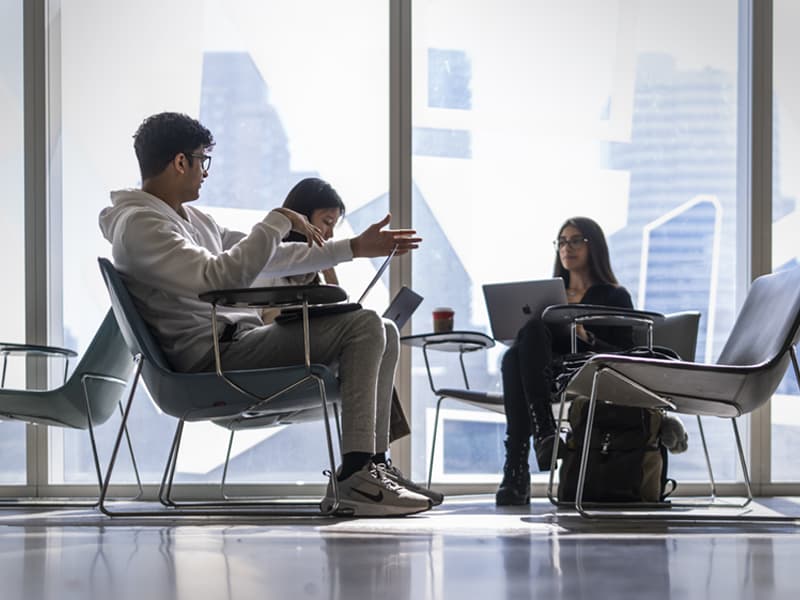 Students sitting and discussing work in a bright campus study space.