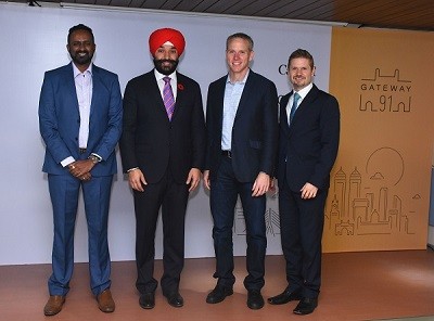 Four professionally dressed individuals stand together at a formal event venue. The group poses for a photo in front of a branded backdrop during a business or networking gathering.