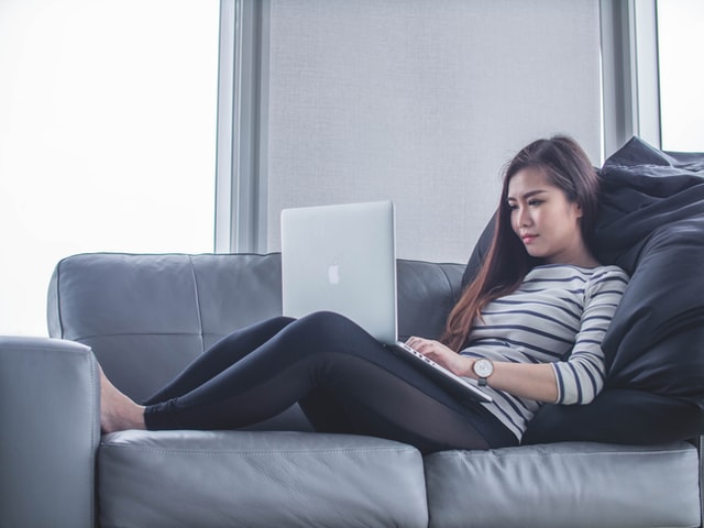 Woman typing at computer laying on couch