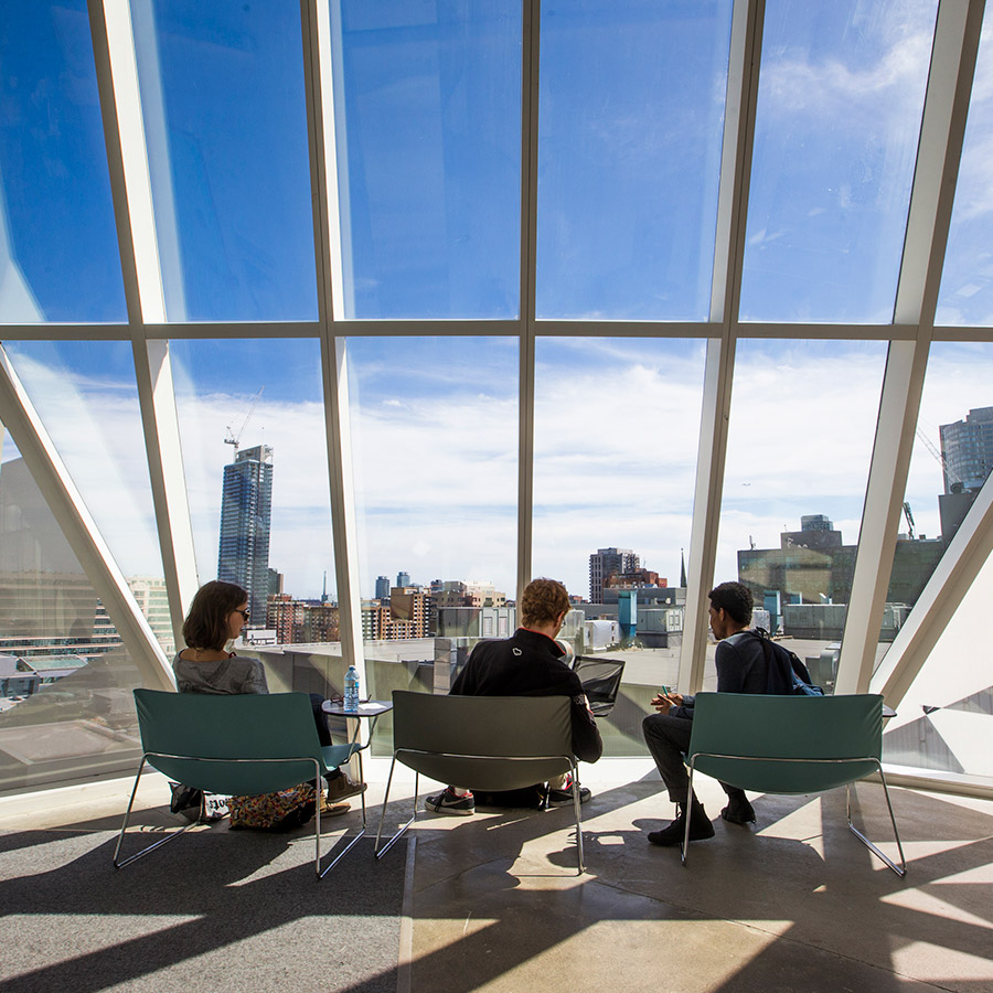 Three students sit by the sunny windows of the SLC.