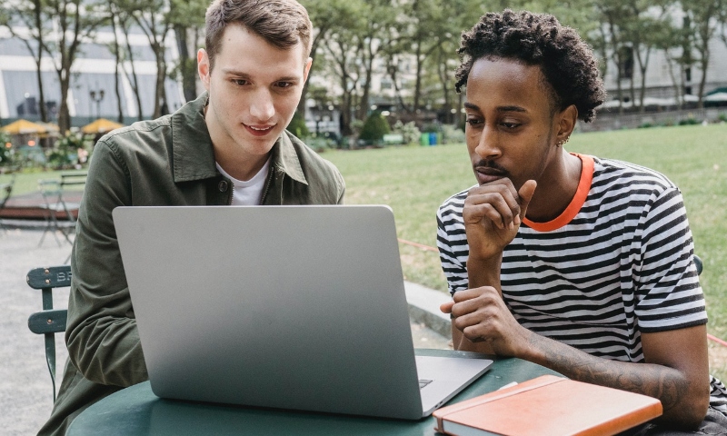 Two male students work on a laptop outside at a table