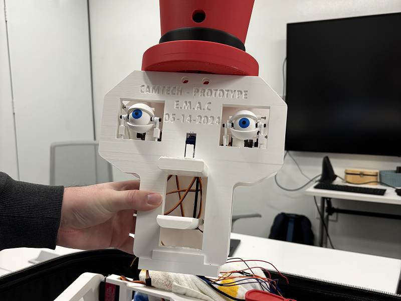Animatronic face wears a red top hat, a hand is holding the robot face upright