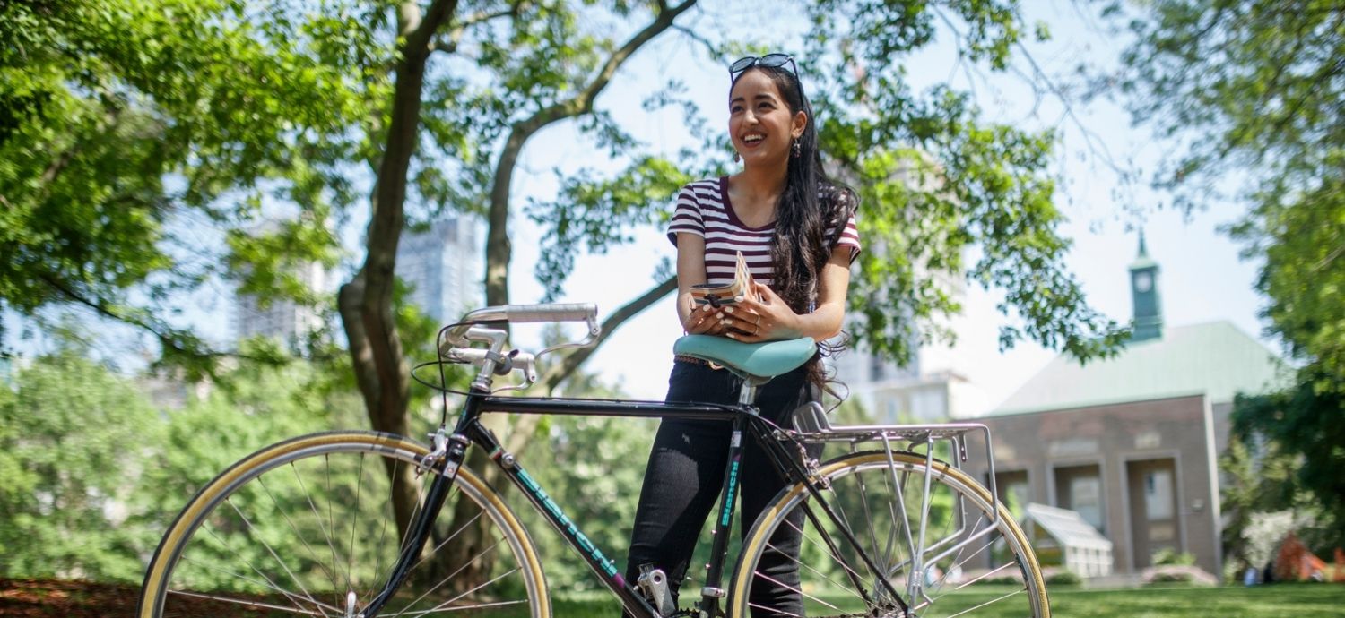 A TMU student stands behind a black and teal bike in the quad.