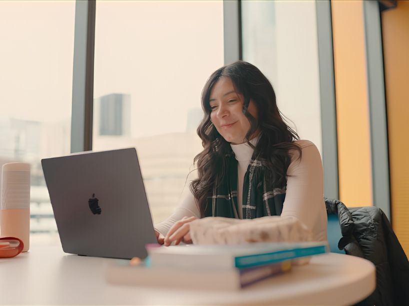 A young woman sitting and looking at a laptop, smiling.