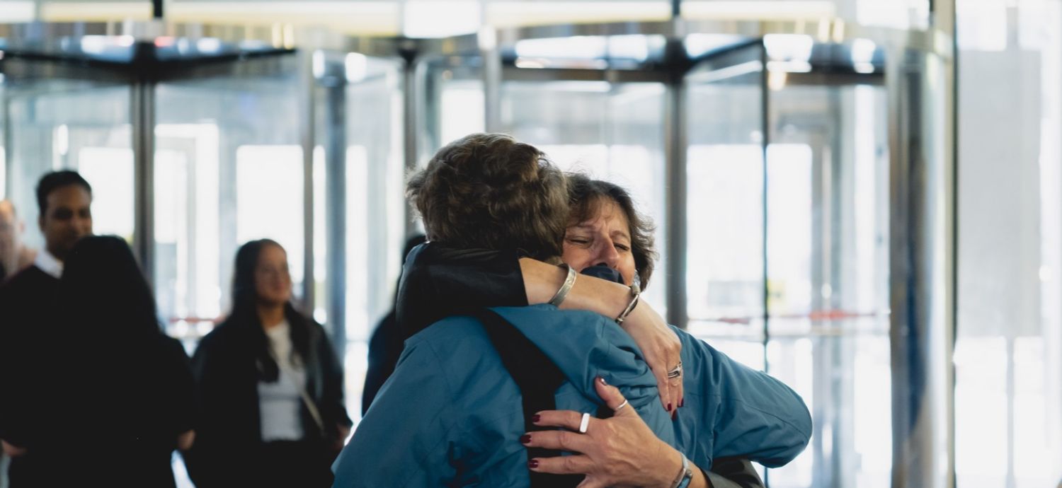 Two women hug; the revolving glass doors of the Student Learning Centre behind them.