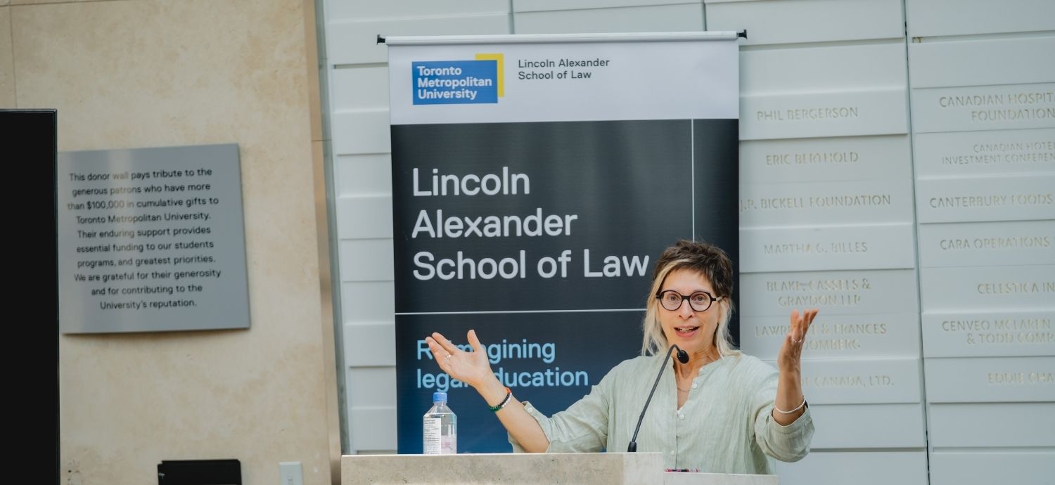 Leilani Farha gestures broadly while speaking from a TMU-branded podium in front of a Lincoln Alexander School of Law banner.