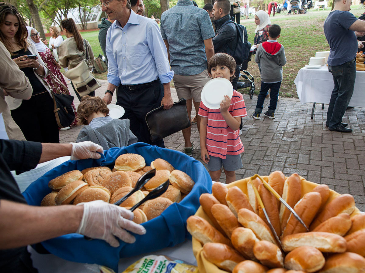 A child holding a plate at a BBQ as someone offers him bread
