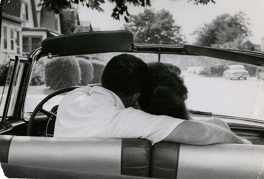 Black and white photo of a man with his arm around a woman, sitting in the car