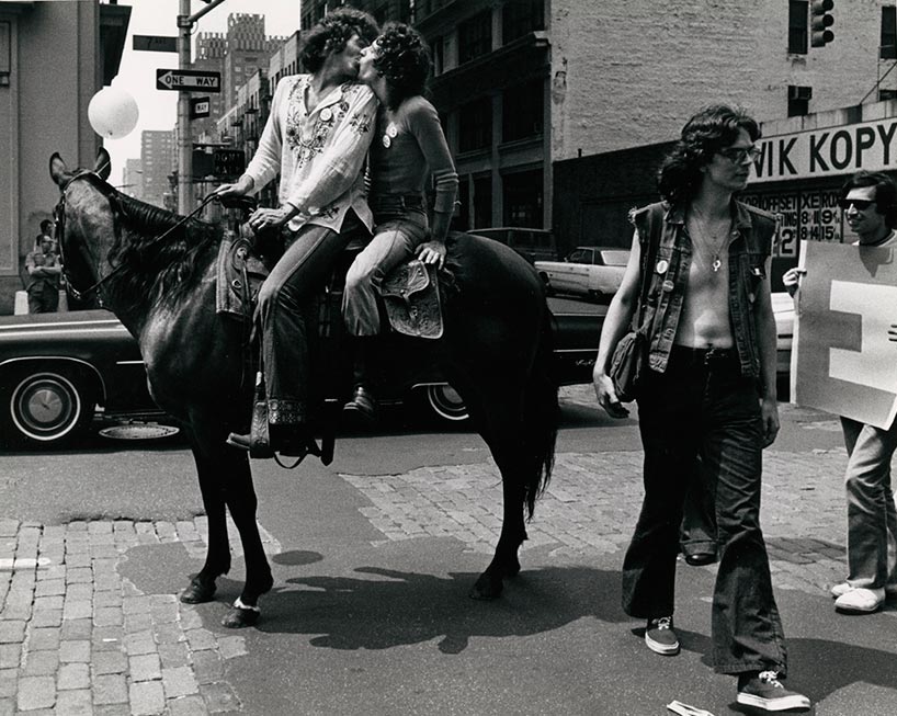 Black and white photo of two men sitting on top of a horse, kissing