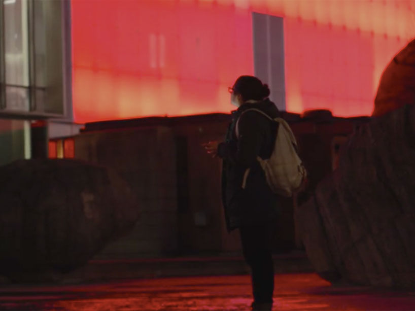 A student looking up at the Ryerson Image Centre lit up in red in honour of missing and murdered Indigenous women