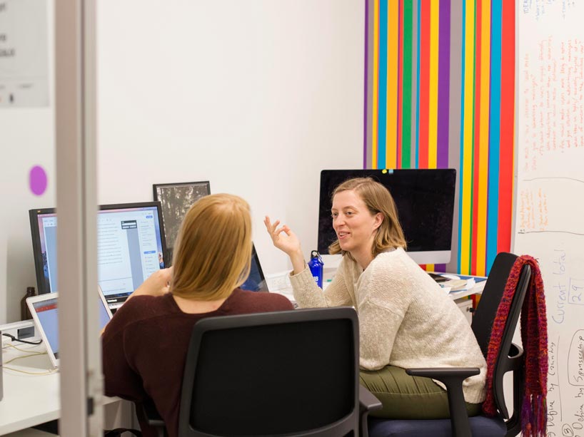 Two people sitting at a computer, talking