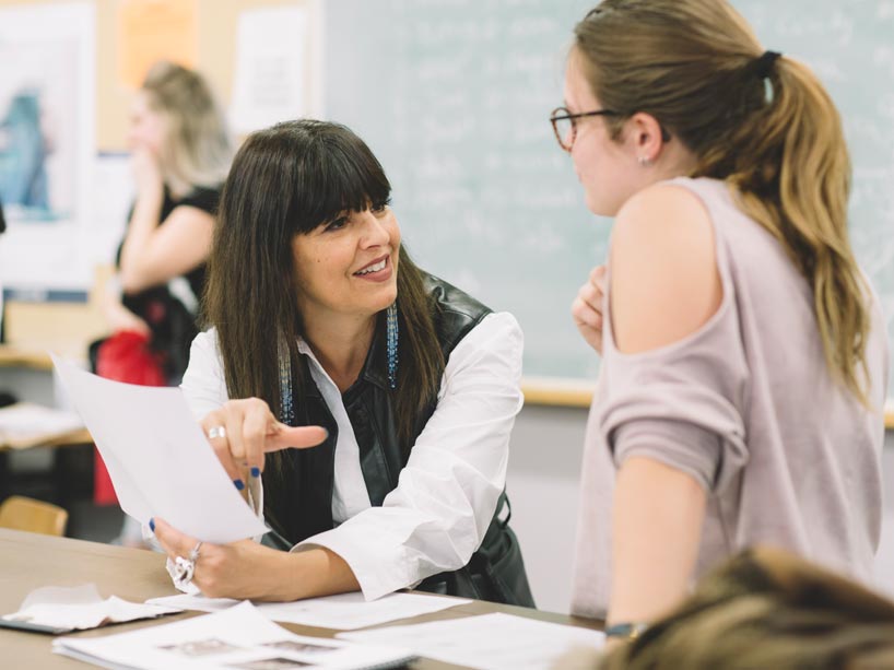 Angela DeMontigny, left, holding a sheet of paper, talking to a female student