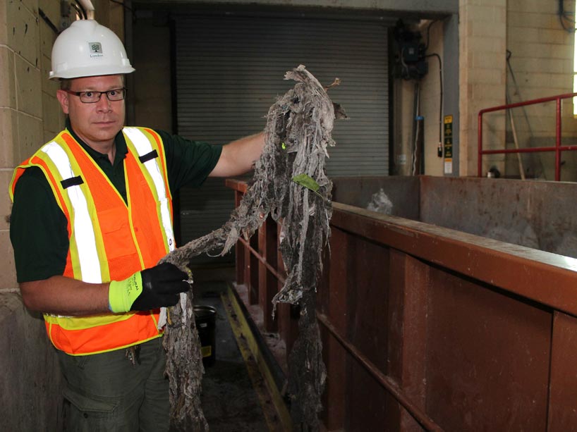 Barry Orr, wearing a hard hat and safety vest, is holding a pile of dirty flushable wipes