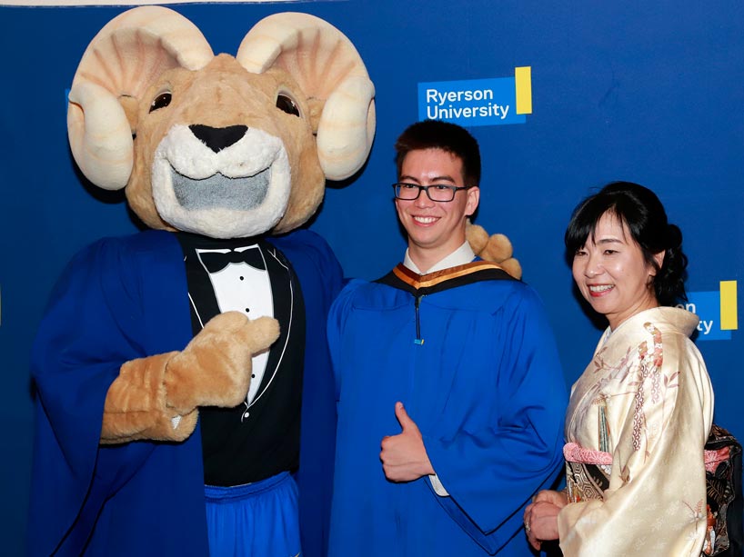 From left: Eggy the Ram pointing to a new grad, centre, who is giving a thumbs up next to a family member