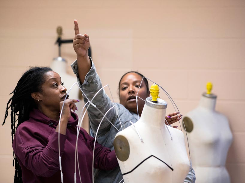 Two women attach a wire frame to a mannequin
