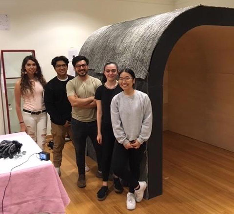 Five people pose in front of a round structure